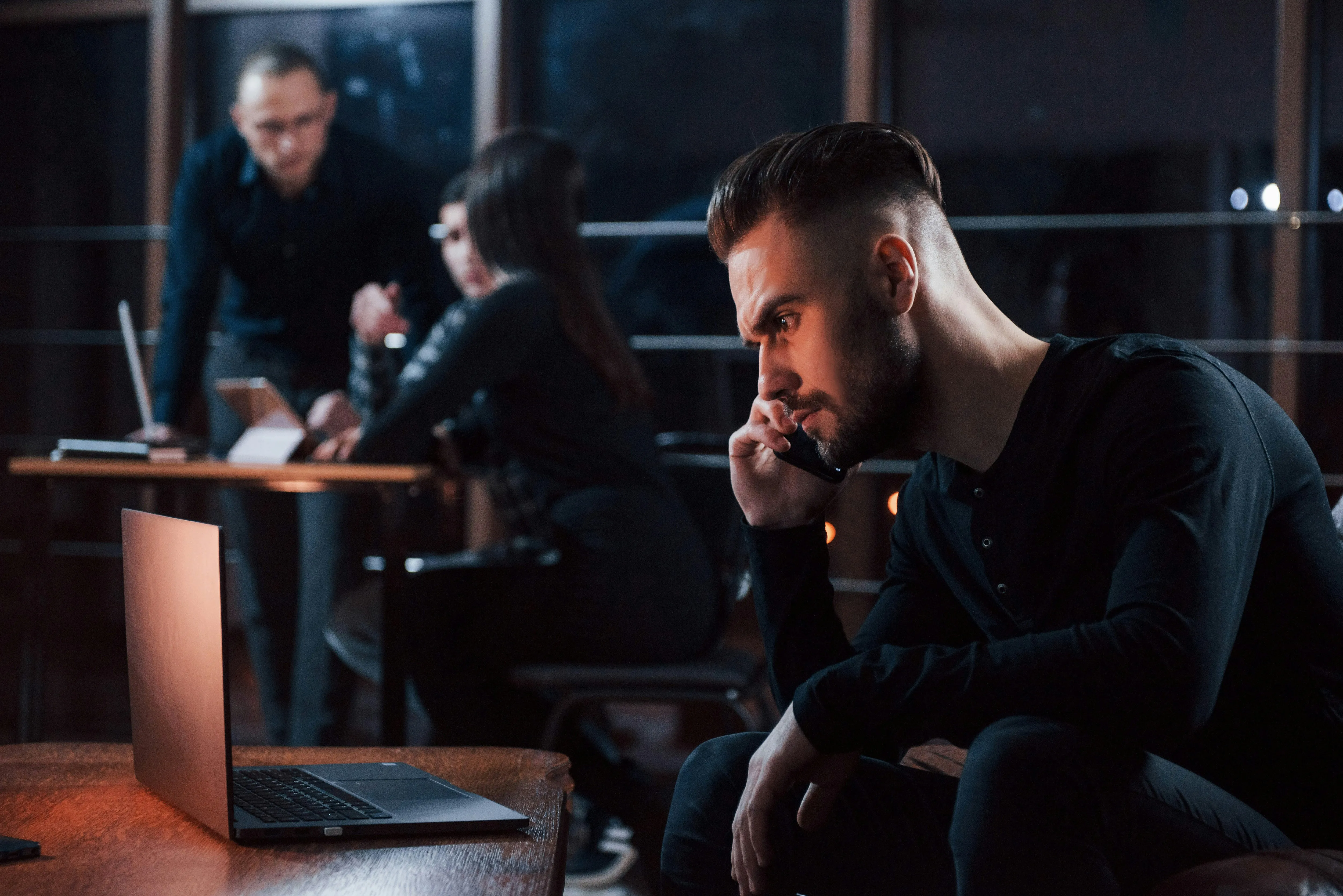 Man, sitting down, on his phone, looking at a laptop